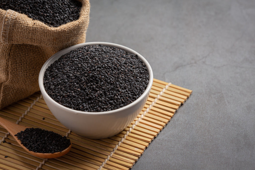 A large bowl of black rice with a half-visible cloth bag filled with uncooked black rice beside it.|一大碗黑米,旁邊是裝有黑米的布袋(部分入鏡)。