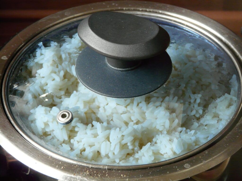 Close-up view through a glass lid showing EatMe parboiled rice simmering and becoming fluffy. 透過玻璃鍋蓋特寫觀察悶煮中的益米預熟米，米粒正在吸收水分並變得蓬鬆熟成。