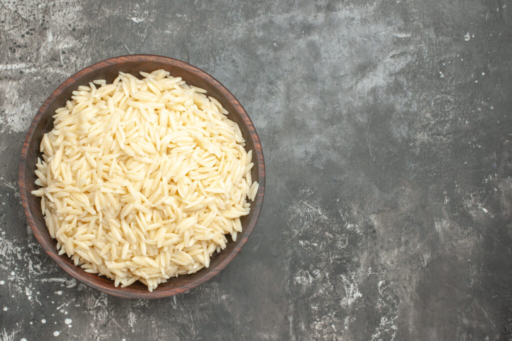 Top view of cooked EatMe parboiled rice piled in a brown ceramic bowl, showing fluffy and separate long-grain texture on a grey background. 俯視圖：盛於棕色陶碗中的益米熟預熟米，展現蓬鬆、粒粒分明的長粒米質感，背景為灰色。