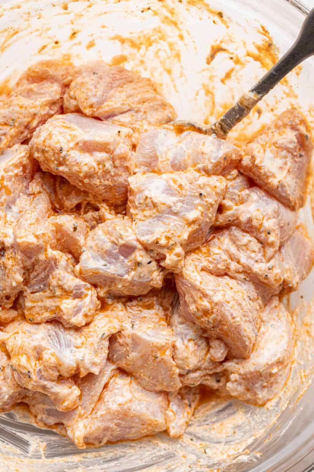 Raw chicken pieces marinated in creamy yogurt and spices in a glass bowl, a key preparation step for making flavorful biryani with parboiled rice. 玻璃碗中以優格與香料醃製的生雞肉塊，是製作風味印度香飯的關鍵備料步驟，搭配預熟米烹調更佳。