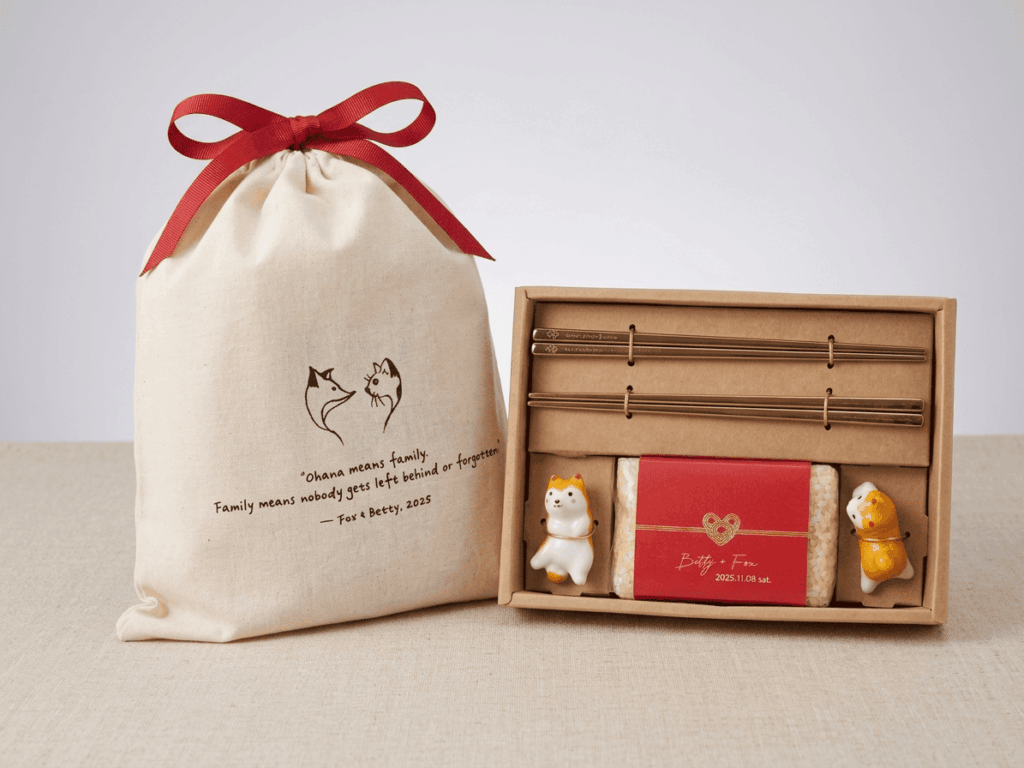 A complete EatMe parboiled rice wedding gift set featuring a personalized red-labeled rice package, a pair of engraved golden chopsticks, ceramic cat chopstick rests, all presented in a kraft gift box with a custom linen drawstring bag tied with a red ribbon. 完整的益米預熟米婚禮禮盒組合，內含客製紅標預熟米、一對刻字金色環保筷、陶瓷貓咪筷架，搭配牛皮紙禮盒與印有新人插圖及文字的亞麻束口袋，以紅色緞帶綁結。