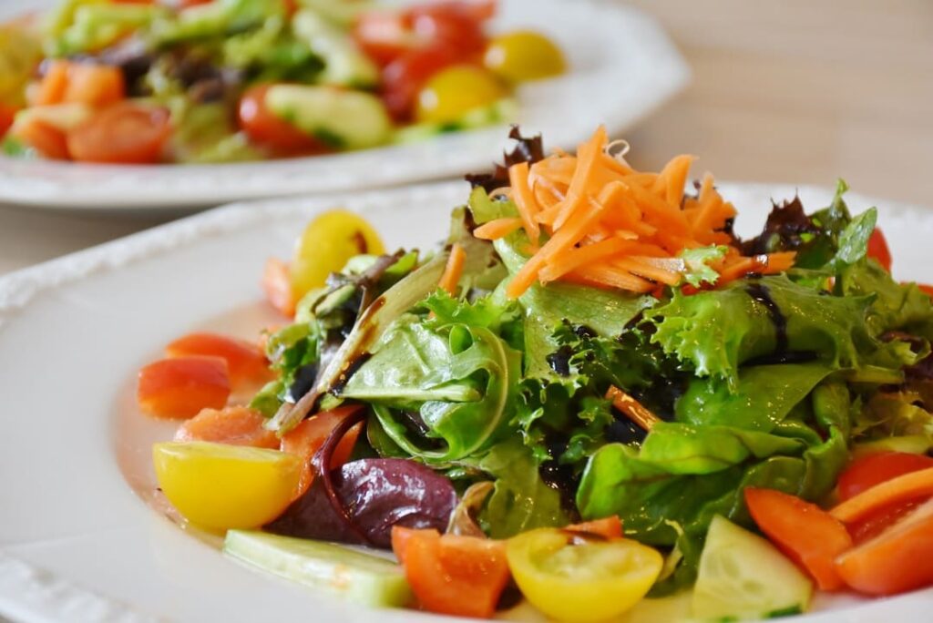 Close-up of a vibrant fresh garden salad with mixed greens, cherry tomatoes, shredded carrots, and cucumber on a white plate — a colorful side dish ideal for pairing with EatMe parboiled rice in a low-calorie balanced meal. 特寫色彩鮮豔的新鮮花園沙拉,白色盤中盛有綜合生菜、小番茄、細絲紅蘿蔔與黃瓜,是搭配益米預熟米低卡均衡餐的理想配菜。
